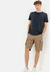 Navy cotton T-shirt paired with light brown cargo shorts featuring multiple pockets. Model wears white sneakers. Simple design, relaxed fit.