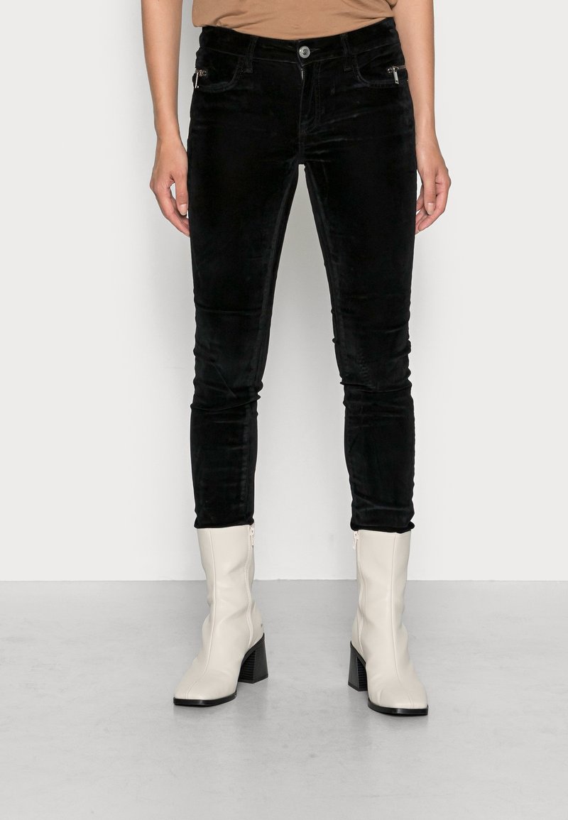 Svarta sammetskinnbyxor med hög midja, med framfickor och en slät yta, ihop med vita ankelskor med klack.