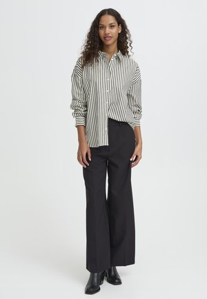 Chemise à rayures verte et blanche, associée à un pantalon large noir taille haute et des bottes à talons noires. Texture de tissu lisse.