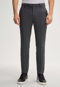 Schlanke graue Hose aus strukturiertem Stoff. Mit flachem Vorderteil, Gürtelschlaufen und seitlichen Taschen, kombiniert mit schwarzen Sneakern.