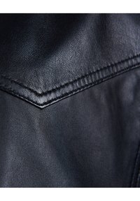 Textur einer schwarzen Lederjacke mit einem auffälligen Nahtdetail und glatter Oberfläche. Das Material hat einen leichten Glanz und eine sichtbare Struktur.