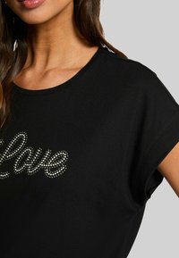 Camiseta negra de manga corta con diseño "Love" en strass plateados. Tela suave con corte relajado y escote amplio.
