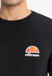 Sweatshirt en coton noir avec un col rond et un logo avec un graphique orange et blanc sur la poitrine gauche. Texture douce.