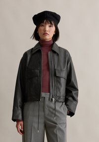 Schwarze Lederjacke mit Reißverschluss vorne, zwei vorderen Taschen und Kragen, kombiniert mit einem kastanienbraunen Rollkragenpullover und grauen Nadelstreifenhosen.