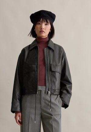 Schwarze Lederjacke mit Reißverschluss vorne, zwei vorderen Taschen und Kragen, kombiniert mit einem kastanienbraunen Rollkragenpullover und grauen Nadelstreifenhosen.