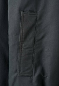 Czarna kurtka z dużą kieszenią o prostokątnym kształcie, wykonana z gładkiego materiału o matowym wykończeniu i widocznymi detalami szwów.