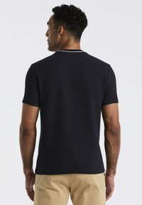 Marineblauw shirt met korte mouwen van een textuurstof, ronde halslijn en subtiele witte stiksels langs de kraag, gecombineerd met khaki broek.