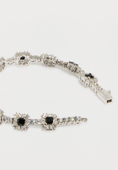 Ασημένιο βραχιόλι με εναλλασσόμενες μαύρες τετράγωνες και καθαρές στρογγυλές πολύτιμες πέτρες, με κούμπωμα σε σχήμα κουτιού χαραγμένο με το όνομα της μάρκας.