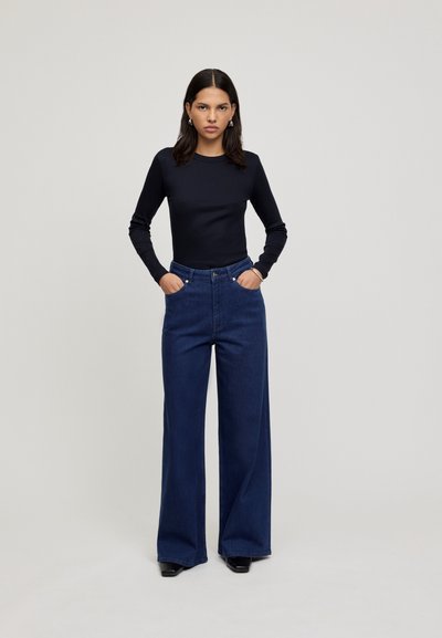 Zwart lange mouwtop gecombineerd met hoge taille, wijde donkere spijkerbroek. De outfit heeft een soepele textuur en een klassieke pasvorm.