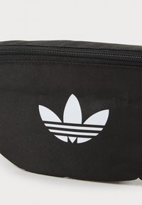 Fekete anyagú derektáska, cipzáros zárással, fehér Adidas logóval, rajta három csíkkal és a háromlevelű formával kiemelten megjelenítve.