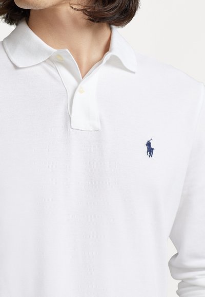 Witte polo shirt van textuurstof, met een klassieke kraag, twee knopen en een klein navy logo op de linkerkant van de borst.