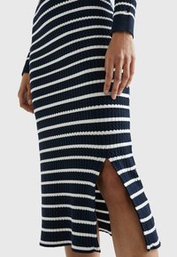 Neulemekko, jossa on tummansinisiä ja valkoisia raitoja, ribbikuviointi, pitkät hihat ja sivureikä lisäyksinä.