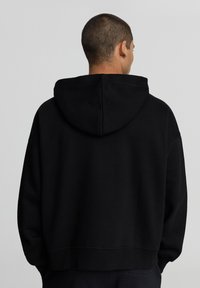 Felpa con cappuccio nera a vestibilità comoda, dotata di un grande cappuccio e polsini a coste. Design semplice, senza motivi o loghi visibili.