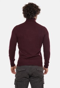 Maglione a collo alto marrone, design aderente con maniche lunghe, polsini e orlo a coste, realizzato in tessuto morbido, texture liscia, senza motivi visibili.