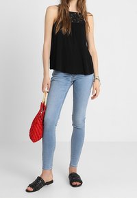 Top negro sin mangas con detalles de encaje, combinado con jeans ajustados azul claro, sandalias de plataforma negras con tachuelas y un bolso rojo de tejido.