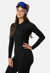 Schwarzes langärmliges Thermoshirt mit gerippter Textur und rundem Halsausschnitt, kombiniert mit schwarzen Leggings und einer rosa Strickmütze mit Logo.