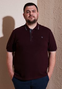 Burgundské polo tričko s dvoubarevnou légou, šedými akcenty na límci a krátkým rukávem. Hladký bavlněný materiál, nošené s tmavými kalhotami.