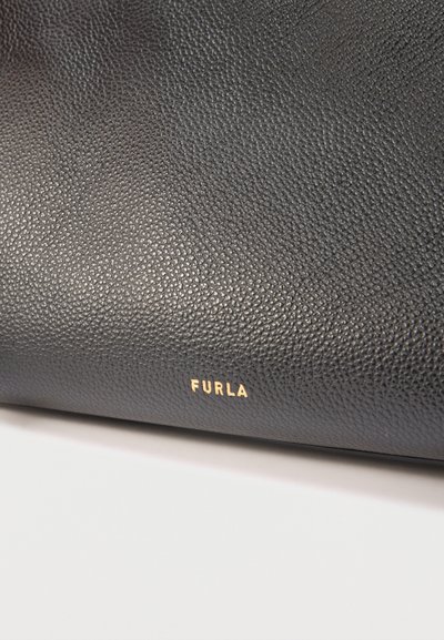 Черна текстурирана кожена повърхност с малък златист надпис „FURLA“, центриран близо до долния ръб на бял фон.