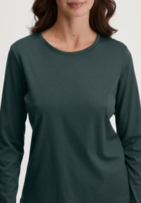Donkergroene blouse met lange mouwen, gemaakt van katoen, met een ronde halslijn en een gladde, zachte textuur. Eenvoudig ontwerp zonder patronen of accenten.