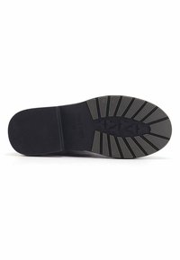 Suola di scarpa nera con una superficie in gomma testurizzata, caratterizzata da righe orizzontali e un logo centrale. Accentuata con un design di battistrada a motivo per una migliore aderenza.