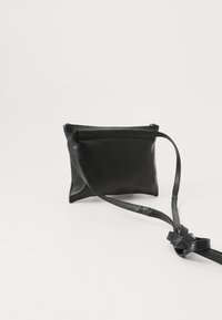 Borsa a tracolla in pelle nera con zip, texture liscia, forma rettangolare e tracolla annodata. Design semplice e minimalista.