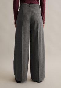 Szerokie, wysokie spodnie w ciemnoszary prążek. Wykonane z teksturowanej tkaniny z pojedynczą kieszenią z tyłu.