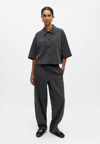 Graues, tailliertes Hemd mit großem Kragen, kombiniert mit locker sitzenden grauen Hosen. Glatte Stofftextur, minimalistisches Design und keine Muster.