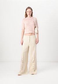 Haut en tricot court rose clair à manches courtes associé à un pantalon large beige orné de motifs floraux brodés près de l'ourlet.