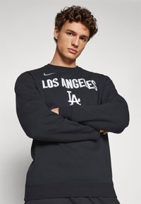 Melnā džemperī ar baltiem uzrakstiem "LOS ANGELES" un "LA", izgatavots no mīksta materiāla, ar klasisku apkakli un ribotām piedurknēm.