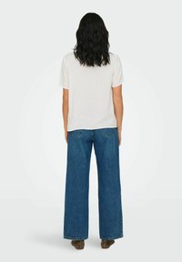 Vit kortärmad topp med subtilt prickmönster, i kombination med vida blå denimjeans. Vy från baksidan. Bruna ankelstövlar.