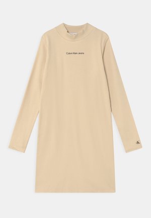 Beżowa, prążkowana sukienka z długim rękawem i stójką, z logo "Calvin Klein Jeans" na piersi oraz małym logo "CK" na mankiecie lewego rękawa.