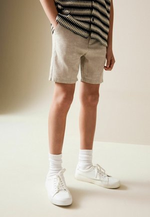Linned-shorts i lys beige med sidelommer, parret med hvide sneakers og ribbede hvide sokker. Sættet har en mønstret skjorte.