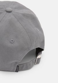 Căciulă de baseball gri fabricată dintr-un material texturat, cu o vizieră curbată, curea ajustabilă la spate și o etichetă mică de brand pe lateral.