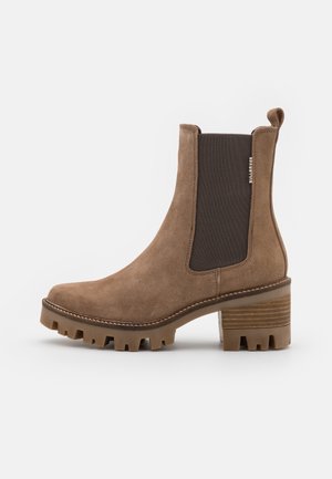 Bottines en daim marron avec des panneaux élastiques sur les côtés, talon empilé et semelle à crampons. Présente des coutures décoratives et une languette à l'arrière.