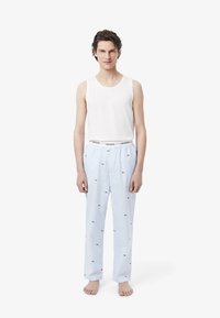 Witte tanktop gecombineerd met blauwe gestreepte pyjamabroek met kleine groene logo's. De stof lijkt zacht en lichtgewicht te zijn.