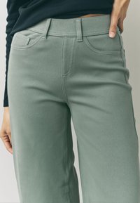 Zelené široké nohavice z bavlnenej zmesi s vysokým pásom, prednými vreckami a jemnými švami. Textúra pôsobí hladko a odolne.