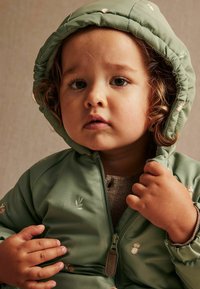 Groene pufferjack met een capuchon, versierd met uilenpatronen en bladdesigns, met een ritssluiting en elastische manchetten. Zacht, glad textuur.