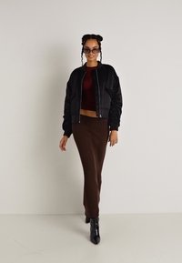 Czarna kurtka bomberka o prążkowanej fakturze, bordowy crop top i brąskowa długa spódnica w prążki. Uzupełnione czarnymi botkami za kostkę i okularami przeciwsłonecznymi.