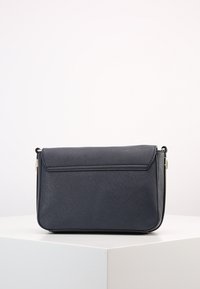 Compact navy blue crossbody bag made of textured synthetic material, featuring a flap closure and gold-tone hardware. Square shape.
