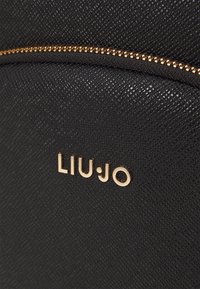 Zwarte tas met textuur, voorzien van een subtiel crisscross-patroon, een ritssluiting in gouden tint en het ingedrukte merksymbool "LIU•JO" aan de voorkant.