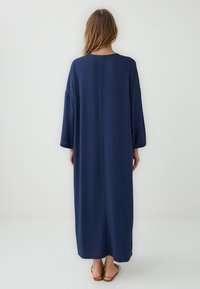 Abito blu navy a maniche lunghe, taglio dritto, realizzato in tessuto leggero, presenta un collo rotondo semplice e arriva sotto le caviglie.