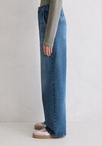 Lichtblauwe hooggesneden denim jeans met een recht gesneden silhouet. Zichtbare stiksels en een middelmatige wassing. Gedragen met witte sneakers.