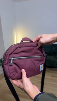 Borsa a tracolla bordeaux in nylon con scomparti con cerniera, tracolla nera, manico superiore e patch con logo Carhartt. Superficie testurizzata e design resistente.