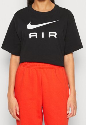 Persoon in een zwart Nike Air t-shirt en felrode elastische broek, zichtbaar van schouders tot halverwege de dij.
