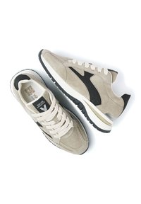 Hellbeige Wildleder-Sneaker mit einem schwarzen Akzent, traditioneller Schnürung und einer Gummisohle mit strukturiertem Profil.