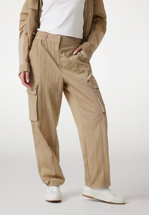 Pantaloni cargo beige realizzati in tessuto stropicciato, con tasche laterali, vita elastica e vestibilità ampia, abbinati a sneakers bianche.