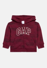 Gyermekek számára készült bordó cipzáras kapucnis pulóver vonatos mintával, elülső zsebekkel és a mellrészen nagy, fehér körvonalas "GAP" logóval.