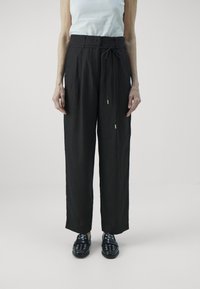 Svarta linnebyxor med vida ben och dragsko i midjan, i kombination med mörka slip-on skor med dekorativa öglor.