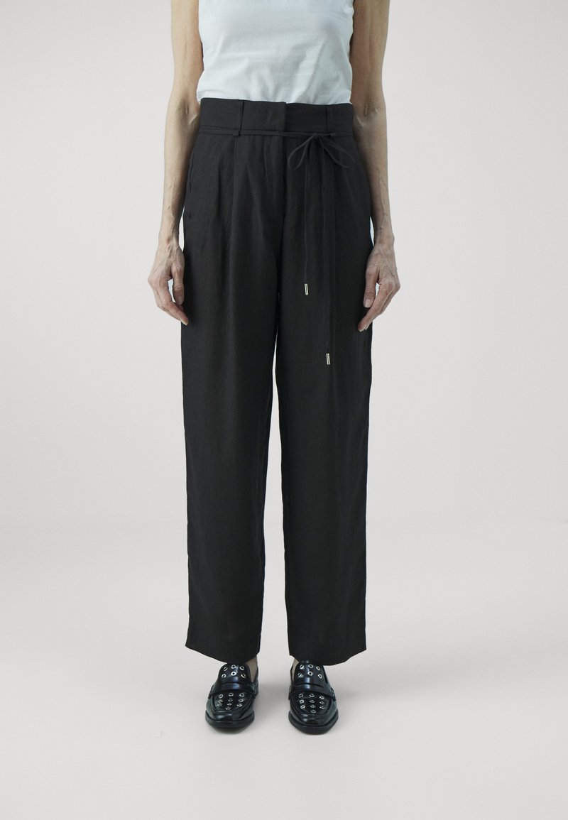 Svarta linnebyxor med vida ben och dragsko i midjan, i kombination med mörka slip-on skor med dekorativa öglor.