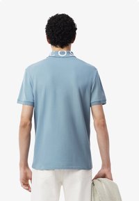 Niebieska koszulka polo z kontrastowym, wzorzystym kołnierzykiem, krótkimi rękawami i gładką teksturą; noszona z jasnymi spodniami i trzymana z dzierganą rzeczą.